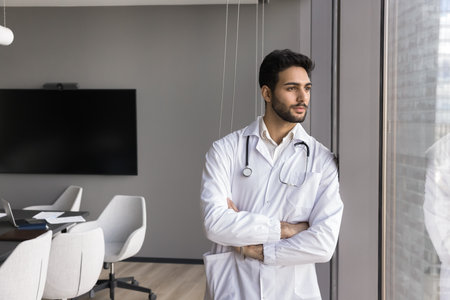 Mission, medical worker career. Serious male doctor in white coat take break, gazing out window standing in conference room after medical council, look in city view, full of aspirations and daydreamsの写真素材
