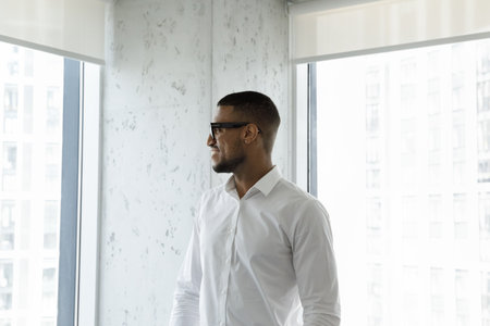 African entrepreneur, employee or company position applicant standing in modern skyscraper office staring at city view feels motivated. Business success, vision, new goals, wealthy lifestyle conceptの写真素材