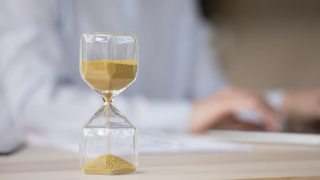 Sand watch object close up with employee human hands typing on laptop in blurred background....