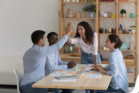 Four enthusiastic multiethnic staff members gather in office board room leaders of team giving high...