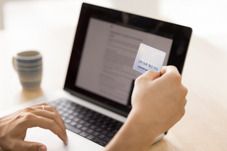 Hands of man holding credit card at laptop with screen view at work table, using financial Internet application, browsing webstores, booking websites for spending money, making transactionの写真素材