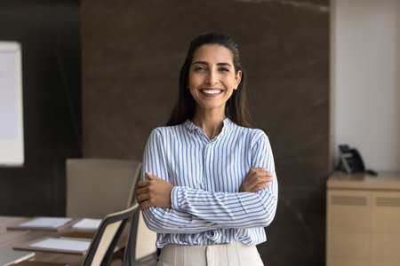 Happy beautiful young Hispanic businesswoman posing in office meeting room alone, looking at camera...