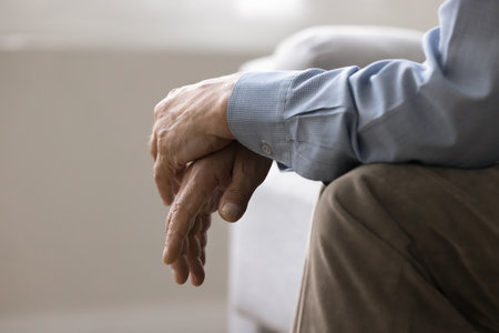 Cropped view, folded hands of unknown senior, man sitting on couch indoors. Close up shot of unrecognizable lonely retired male, deep in thoughts about senile diseases, loneliness in nursing houseの写真素材