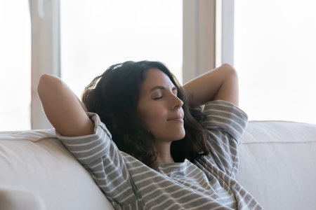 Beautiful woman relax on sofa with hands behind head, close up, spend carefree weekend leisure alone, enjoy silence, air conditioning system inside, quiet house appliances at home. Daydreams conceptの写真素材