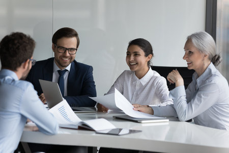 Happy different aged diverse business group negotiating on marketing reports, talking, discussing startup project strategy, laughing, brainstorming. HR team interviewing job candidateの写真素材