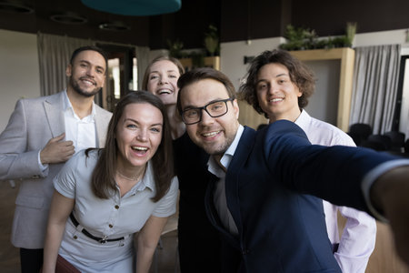 Excited joyful business group celebrating corporate success, high teamwork result, team achieve, feeling joy, having fun, looking at camera, smiling, taking selfie. Office self portraitの写真素材