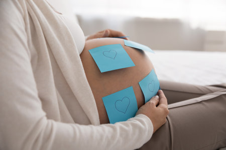 Close up cropped shot unknown pregnant woman touch her big bare belly with attached blue post-it...