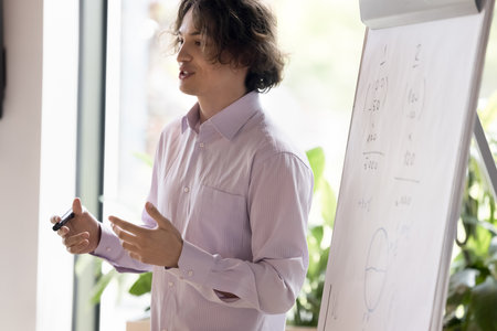 Happy motivated business project leader man speaking at flipchart, presenting sales reports, calculations, talking to colleagues on corporate meeting. Young teacher, mentor training internsの写真素材
