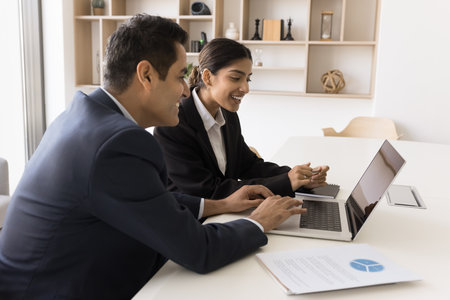 Experienced Indian male employee manager executive mentoring coaching female intern trainee on workplace teach to use corporate software. Diverse coworkers cooperate prepare document report on laptopの写真素材