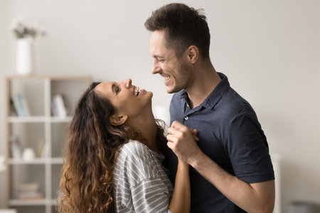 Joyful young couple in love hugging and dancing at home, talking, holding hands, laughing, enjoying romantic leisure time, activity, entertainment together, discussing good newsの写真素材
