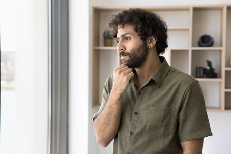Pensive young businessman of Arabic ethnicity lost in thoughts try to predict future sales result. Thoughtful male financial analyst hesitate pondering on new possibilities of risky business solutionの写真素材