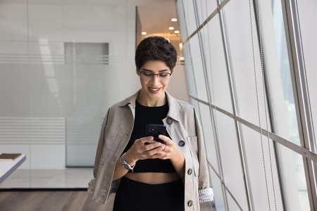 Positive mid adult entrepreneur woman in casual typing on mobile phone in office business space alone, using online financial web service, Internet platform, browsing social media networkの写真素材