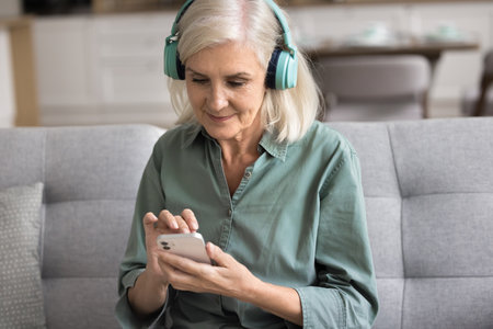 Focused attractive woman wear modern wireless headphones listen music, choose song using mobile...