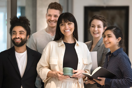 Happy diverse office team with mature female Latin leader standing together, looking away, smiling,...