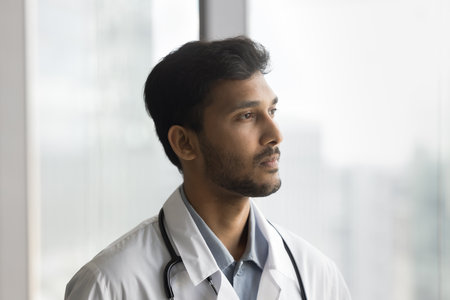 Pensive male doctor private practice owner stand by window at cabinet focus on new idea for healthcare service. Young physician doc think about professional development solve problem challenge in mindの写真素材