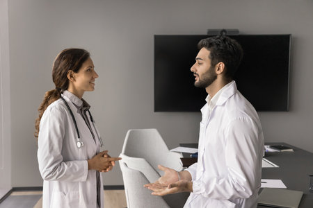Two doctors colleagues of diverse gender ethnicity talk at healthcare center boardroom hold...