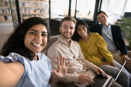Happy young Indian manager girl in casual taking selfie with office friends, business colleagues...