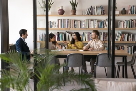 Diverse students discussing training project in academic meeting room interior, talking in library,...