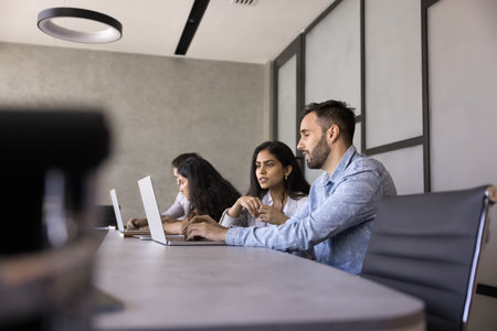 Couple of diverse young business colleagues working at laptop together, talking at computer in...