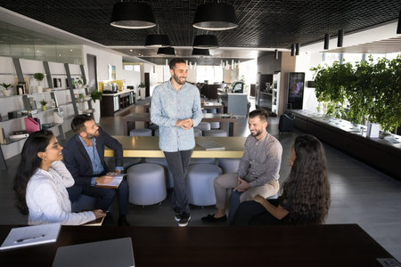 Diverse business group of happy coworkers and male leader talking in modern workspace, meeting in...