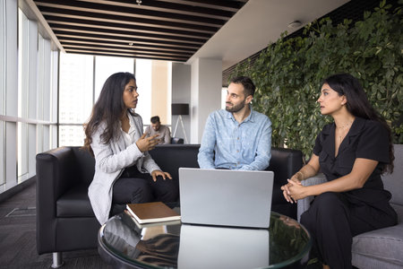 Diverse business group of young colleagues talking on co-working space, sitting on couch in office...
