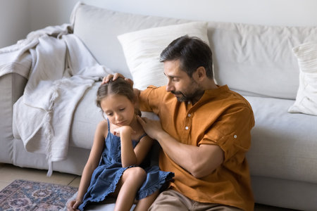 Sympathetic middle aged Latin dad comforting sad little daughter kid, stroking, head, consoling child at home, giving support, love, care. Hispanic father talking to cute frustrated offended childの写真素材