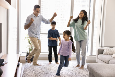 Couple of cheerful Indian parents and two active sibling kids dancing to music on carpet in living room, enjoying songs, activity, funny family party, leisure, smiling, laughing. Full length shotの写真素材