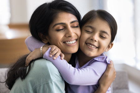 Happy caring young Indian mom hugging cute preschool daughter kid with faces touch, keeping eyes closed, embracing child with love ,devotion, affection, enjoying motherhood, family bondingの写真素材