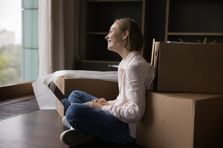 Cheerful dreamy homeowner woman searching web for new home, relocation service, transportation...