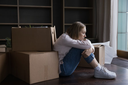 Frustrated tired former homeowner woman moving out from apartment, sitting at heap of stacked boxes, paper containers, feeling frustrated about eviction, bankruptcy, mortgage defaultの写真素材