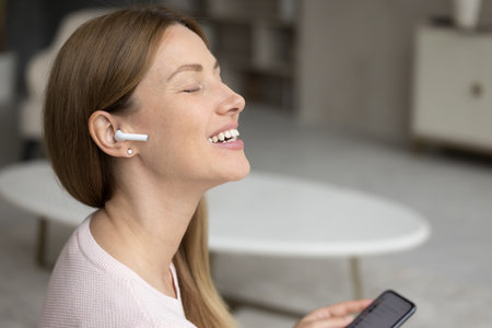 Happy excited millennial woman listening to inspiring music from wireless earphone in ear, enjoying...