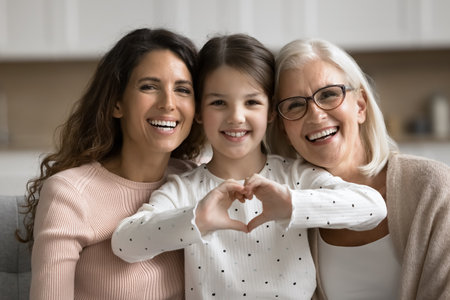 Portrait of cute little 6s girl showing love symbol with joined fingers, posing for camera with older granny and young mum. Strong family bonds, love across generations and emotional connection, careの写真素材