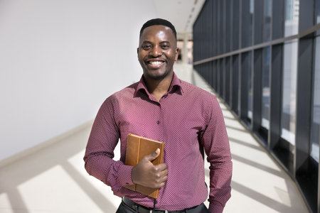 Cheerful ambitious young African American company CEO man posing for corporate portrait in contemporary office hallway alone, looking at camera, enjoying business leadership, successful careerの写真素材