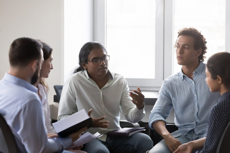 Employees discuss business ideas at office briefing, Indian male team leader or coach give professional advice to diverse staff members, take part in corporate training, counsel, mentoring conceptの写真素材