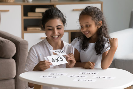 Happy Indian daycare teacher showing flash cards to little kid, helping child with multiplication...
