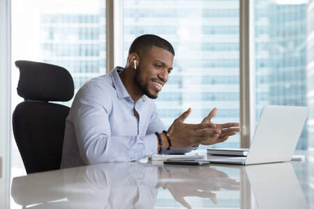 Happy inspired millennial Black business man speaking on video call at laptop, using wireless...