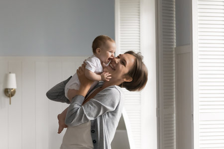 Sweet moments of parenting. Happy affectionate young mom hug small baby child play with beloved infant at light cozy living room raise kid up hold in arms with warmth care enjoy motherhood. Copy space