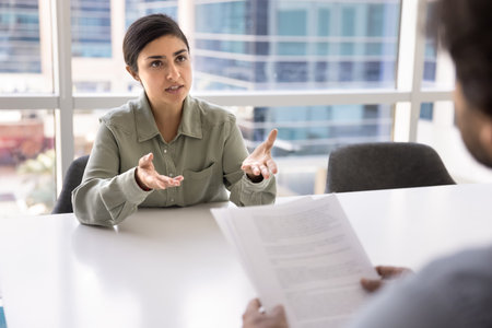 Serious beautiful young businesswoman talking to male business colleague at meeting table, speaking...