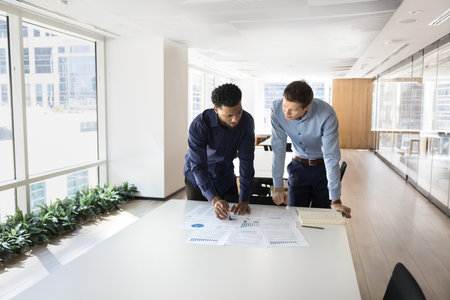 Focused busy multiethnic male professionals working on project reports together, analyzing marketing...