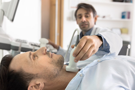 Close up of male patient lying on clinic couch during ultrasound scanning procedure. Sonographer doctor examining man for thyroid disease, throat, linph nodes, applying scanner to neckの写真素材