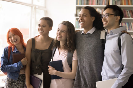 Sense of team. Group of happy motivated multiethnic teenage college pupils high school students standing in row hugging mates shoulders smiling looking at distance laughing feeling trust support unityの写真素材