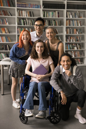 Inclusion and diversity. Vertical shot happy diverse polyethnic students group posing for portrait. Smiling teen female on wheelchair look at camera together with friendly supportive mates at libraryの写真素材