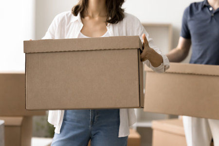 Close up cropped view of young married couple holding big cardboard boxes standing together indoors on relocation. Renovation, repairs works, new home buying, transporting services ad on moving dayの写真素材