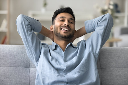 Peace of mind. Head shot portrait serene carefree young man relax on sofa with candid smile in calm lazy mood having pleasure breath deep with cool fresh conditioned air chill alone on weekend day offの写真素材