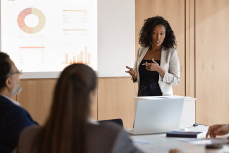 Serious confident African American speaker giving training seminar to team of coworkers, speaking at board, presenting sales growth report, analytic data, telling project plan, strategyの写真素材