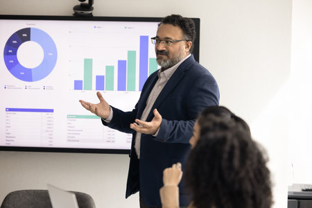 Mature Indian company CEO presenting sales growth analytics to group of employees, colleagues,...