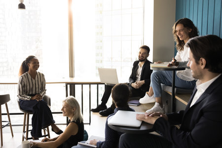 Six professionals engaged in lively and informal meeting in modern office, having friendly conversation seated on tiered, enjoy relaxed and collaborative atmosphere, interacting positively. Seminarの写真素材