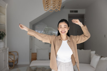Cheerful beautiful 20s Asian girl dancing at new home, having fun, laughing, enjoying disco music, party, activity, leisure in dwelling living room, celebrating successの写真素材