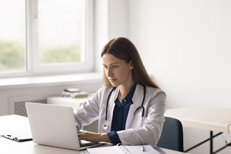 Work day of doctor. Focused woman medic worker using notebook computer at workplace in hospital cabinet type medical records do electronic paperwork make research browse information online. Copy spaceの写真素材