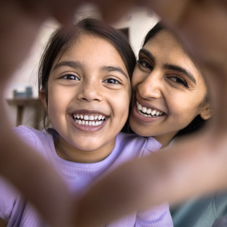 Close up faces through joined finger showing Indian woman and her adorable little 5s daughter stare at camera revealing white teeth. I love you, declaration of loveの写真素材